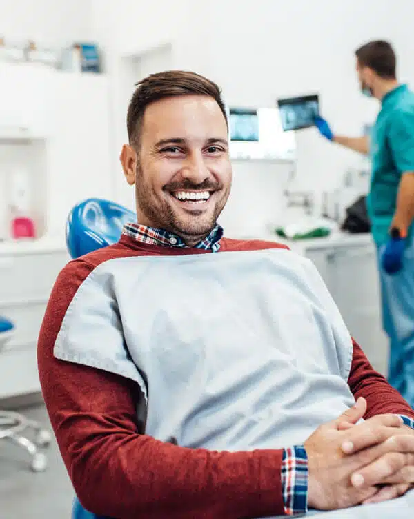 Smiling man in dental office with staff working in background at Shelton Dental Excellence.