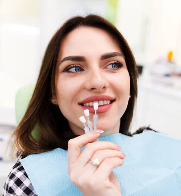 Young woman smiling at dental office, holding toothbrush near mouth, wearing checkered shirt.